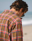 Man wearing a the brown/red bucky flannel on a beach.