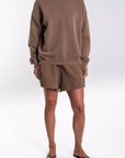 Woman wearing a brownstone french terry sweatshirt and day shorts set on a white background