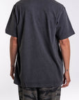 Back view of a woman wearing a dark gray t-shirt and camouflage pants on a white background