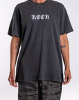 Person wearing a black graphic t-shirt with 'KOOK' logo and camouflage pants on a white background