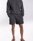 Person wearing a dark gray french terry sweatshirt and day shorts set on a white background