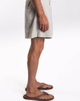 Side view of a person wearing light-colored shorts and sandals on a white background