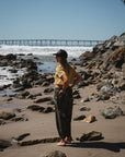 woman wearing beach crop t-shirt in sunrise yellow with real tree camo day pants and surf trucker hat