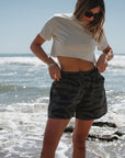 woman wearing beach crop t-shirt in sandstone with ocean tiger camo day shorts at the beach