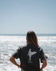 woman wearing surfer girl graphic t-shirt showing back of the shirt on a beach