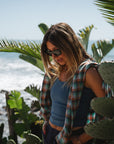 woman near plants at the beach wearing surf tank in blue wave with summer softy flannel in green/orange over her shoulders