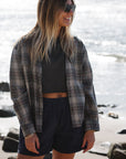 woman wearing summer softy plaid shirt in black/red with beach crop tee in sea grey and navy day shorts at the beach