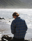 man walking away with blue/black Bucky flannel overshirt at the beach