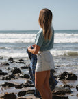 woman wearing beach crop t-shirt in ocean holding the Bucky Blue/black flannel with denim day skirt on a beach