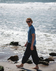 man walking on the beach. he is wearing beach t-shirt in teal with navy day pants.