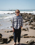 man wearing blue/tan bucky flannel over shirt with navy day pants at the beach
