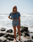 woman wearing beach crop t-shirt in blue wave with denim shorts and beach bandana on a beach