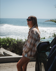 Woman standing by a car near the ocean with sunglasses on wearing Bucky Split Hem Shirt Jacket in Beige/Plaid