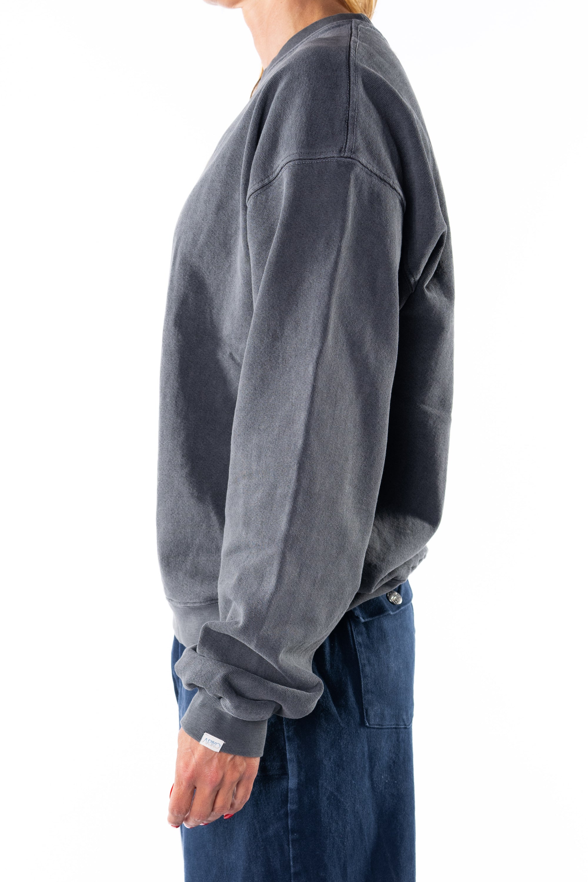 Side view of a woman wearing a gray sweatshirt and navy day pants on a white background