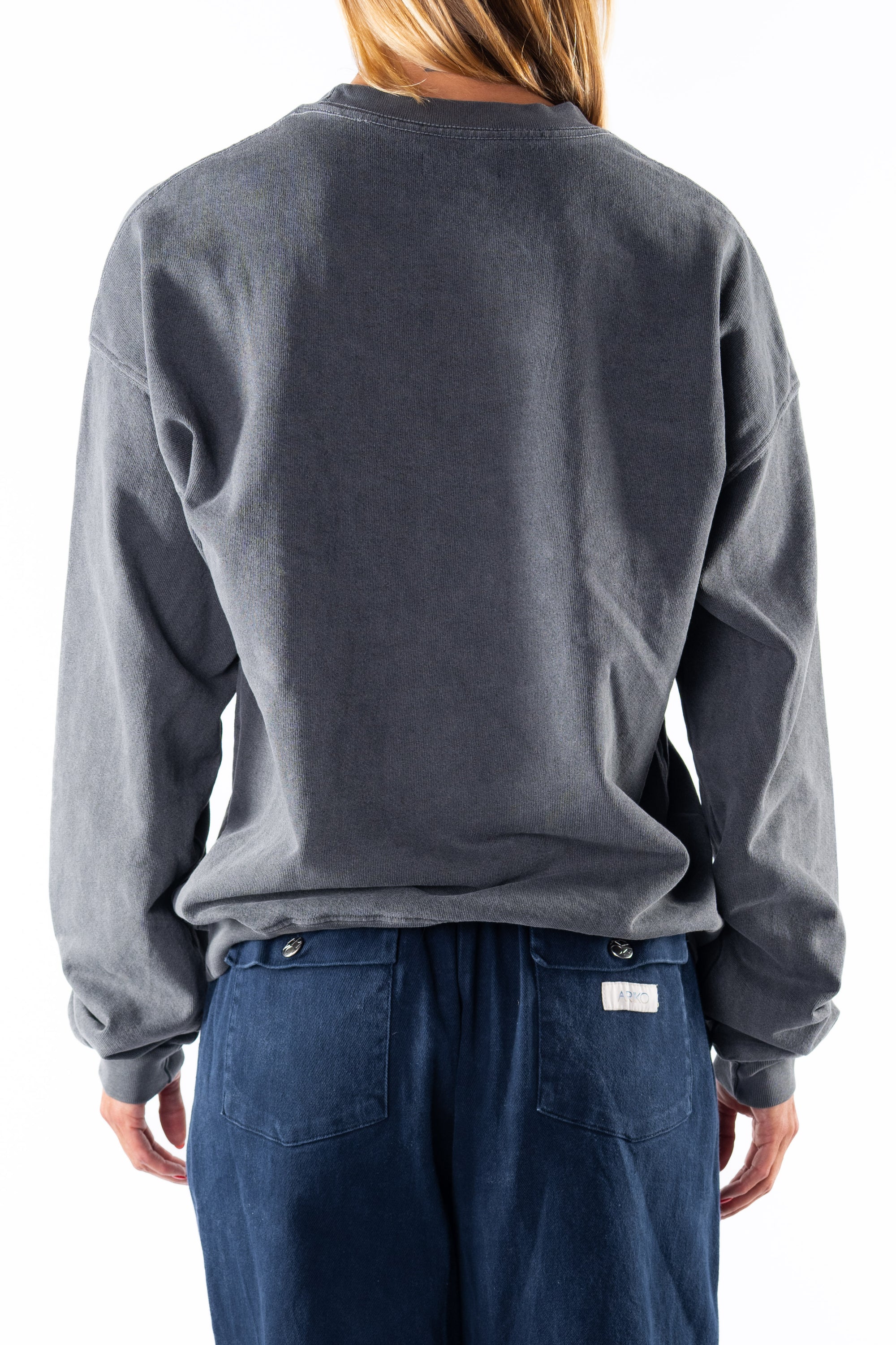 Back view of a woman wearing a gray sweatshirt and navy day pants on a white background