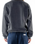 Back view of a woman wearing a dark gray sweatshirt and navy day pants on a white background