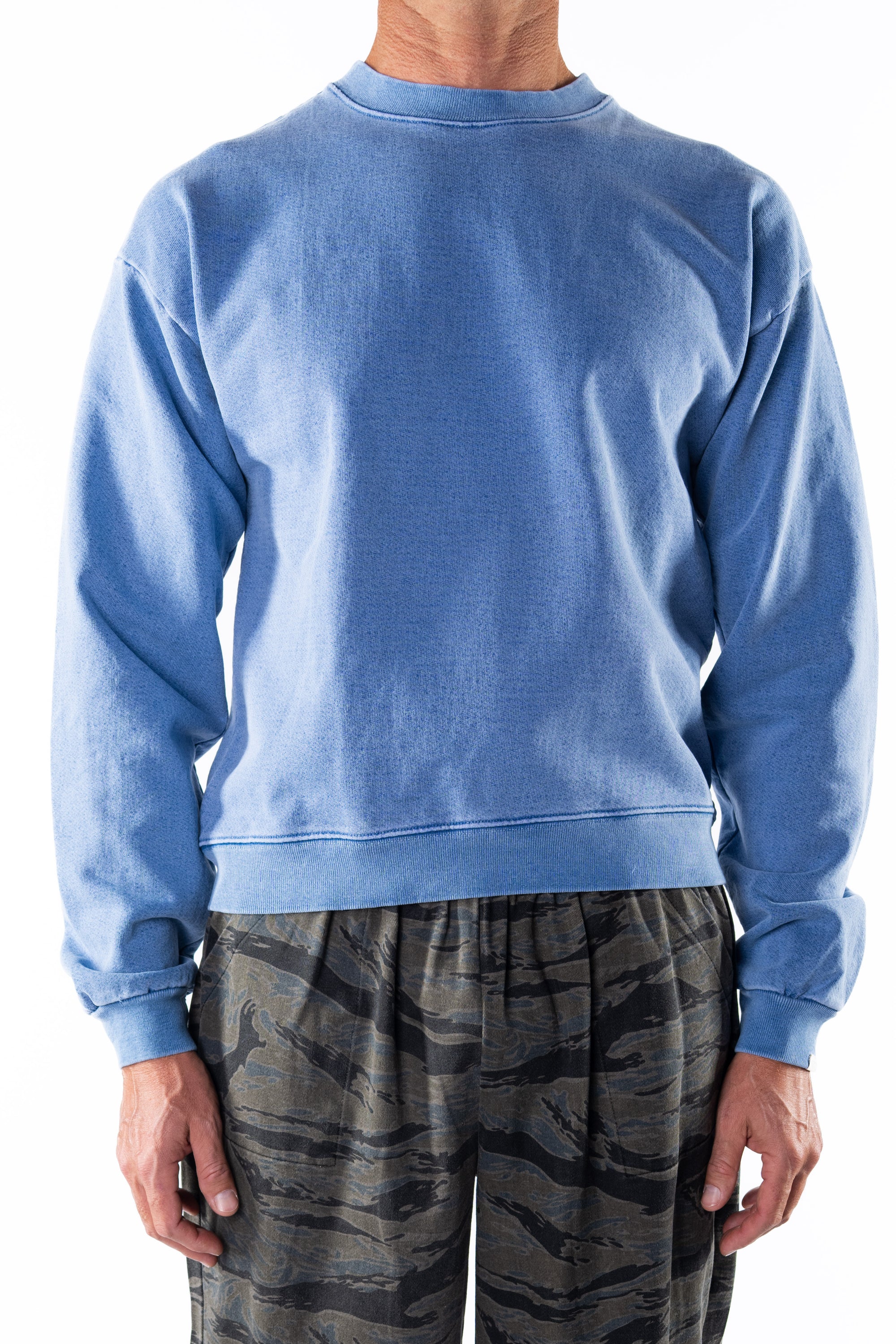 Person wearing a blue sweatshirt and ocean tiger camo day pants on a white background