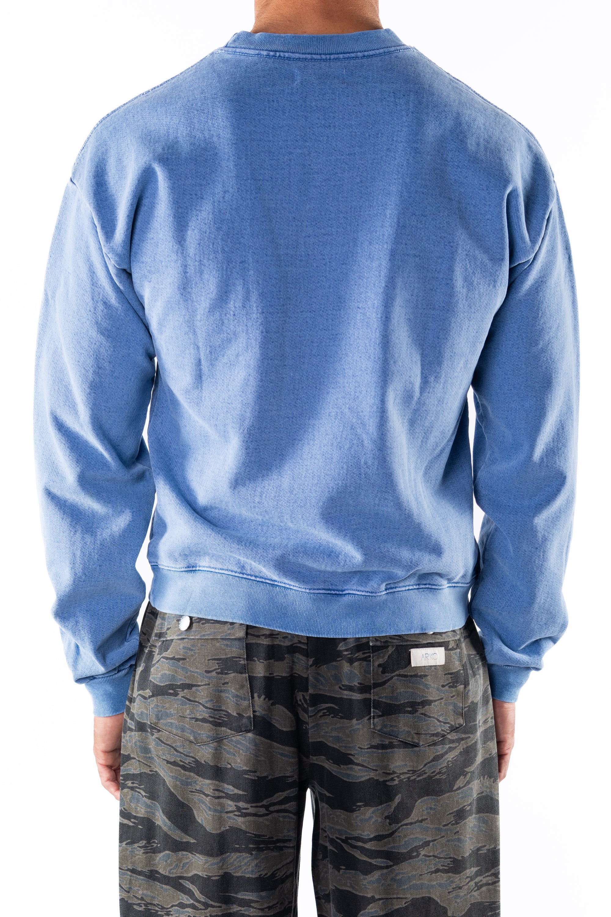 Back view of a person wearing a blue sweatshirt and ocean tiger camo day pants on a white background