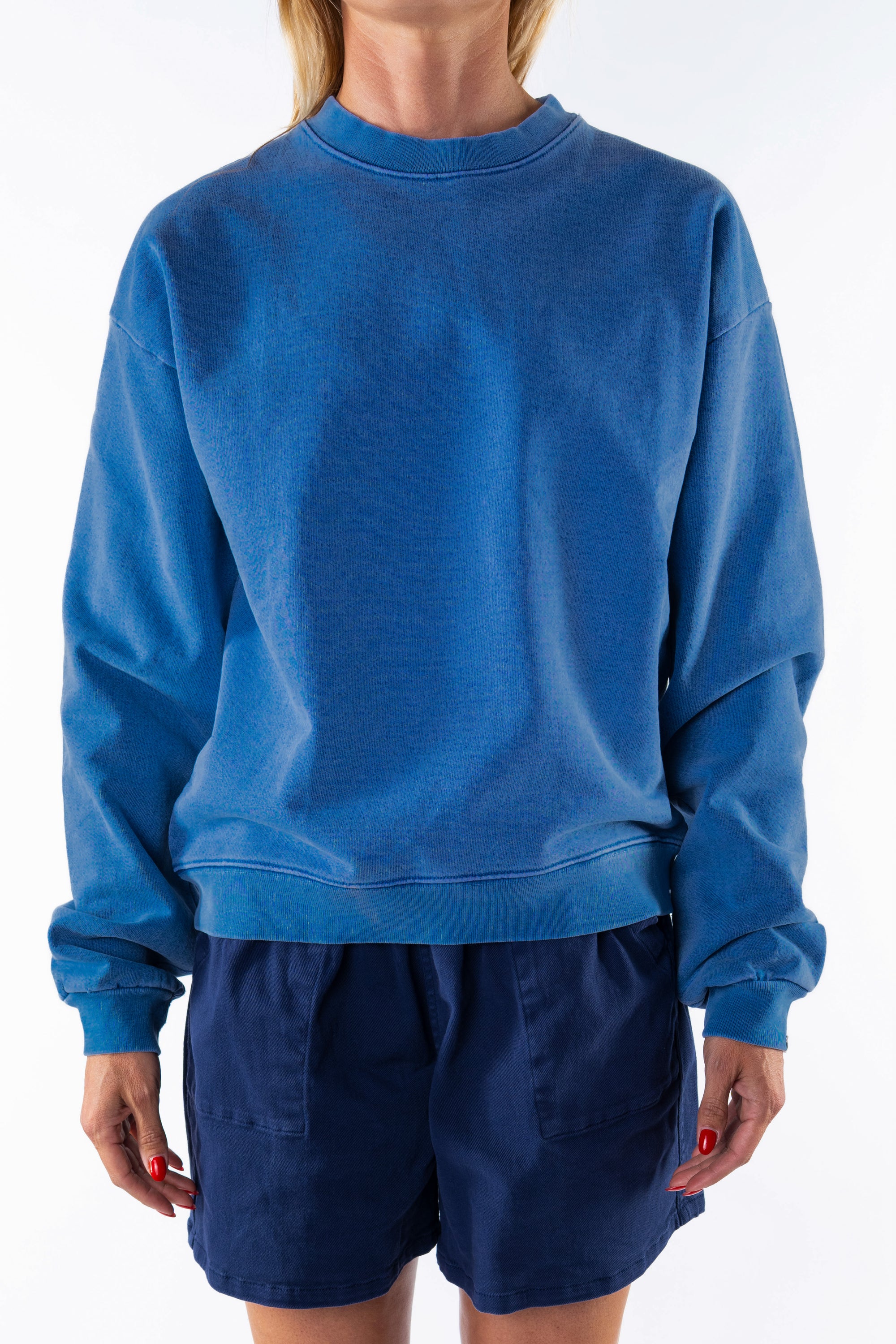 Person wearing a blue post surf crew sweatshirt and navy day shorts on a white background