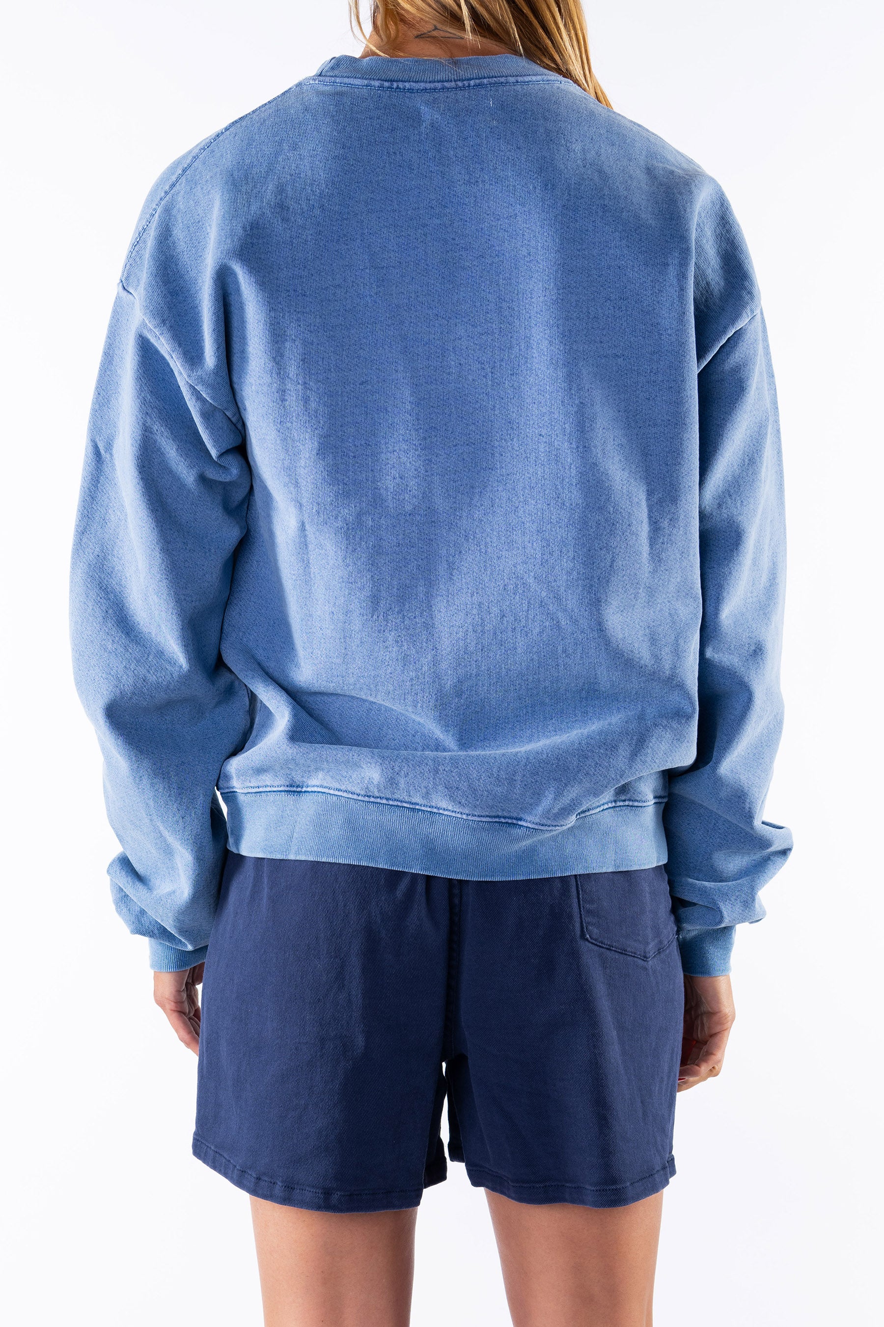 Back view of a woman wearing a blue sweatshirt and navy shorts on a white background