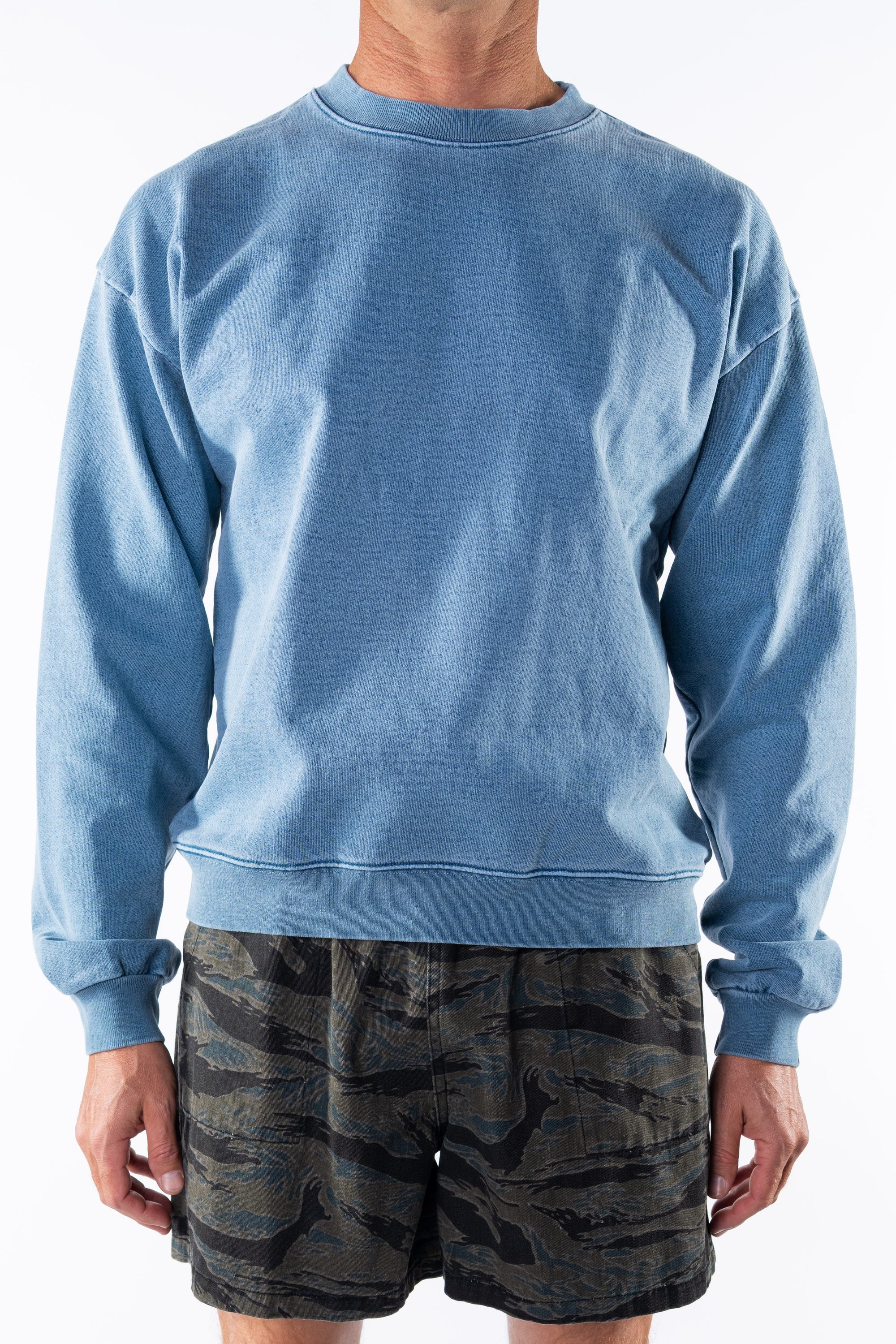 Person wearing a teal sweatshirt and ocean tiger camo day shorts on a white background