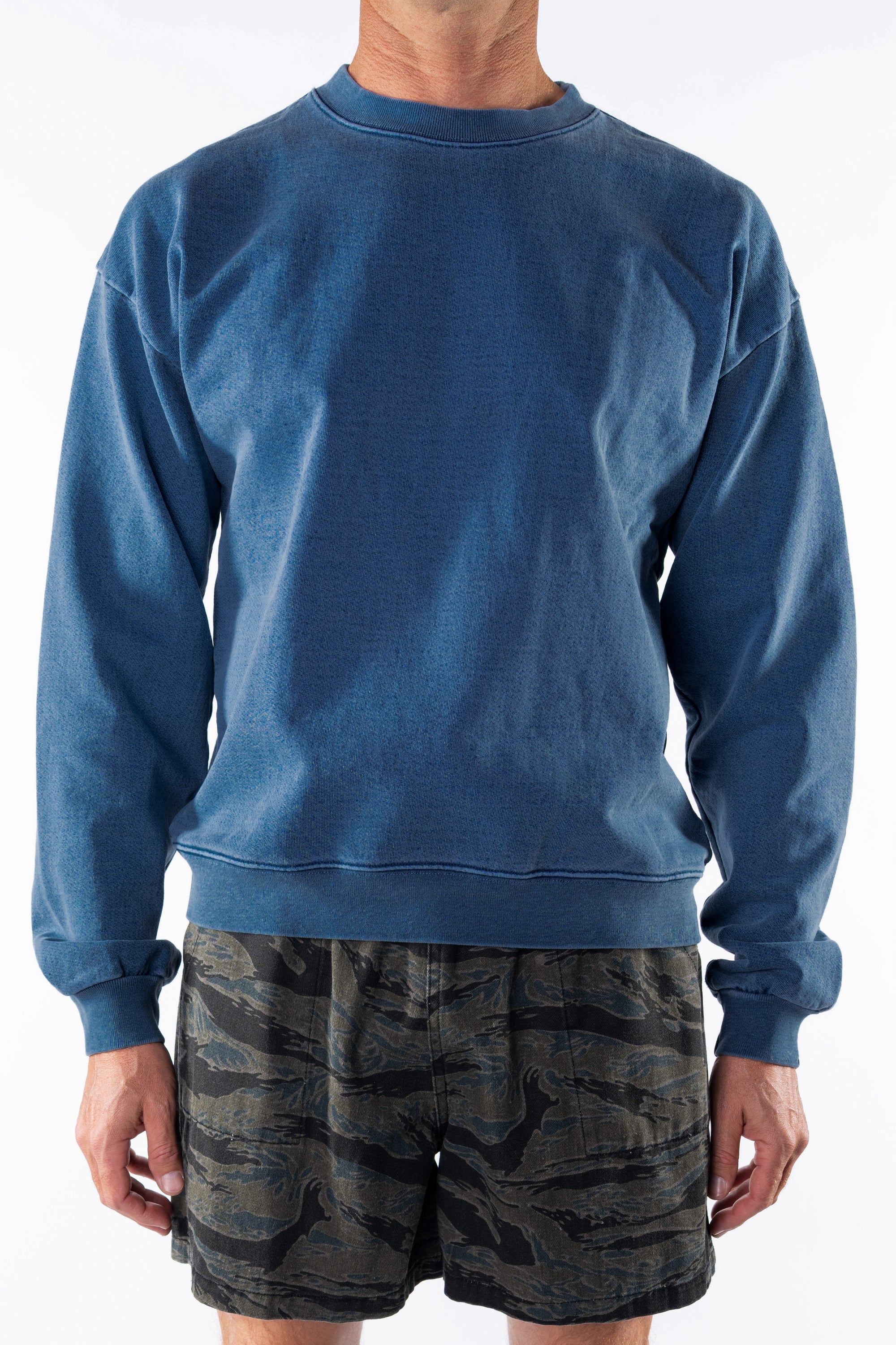 Person wearing a teal post surf crew sweatshirt and ocean tiger camouflage day shorts on a white background