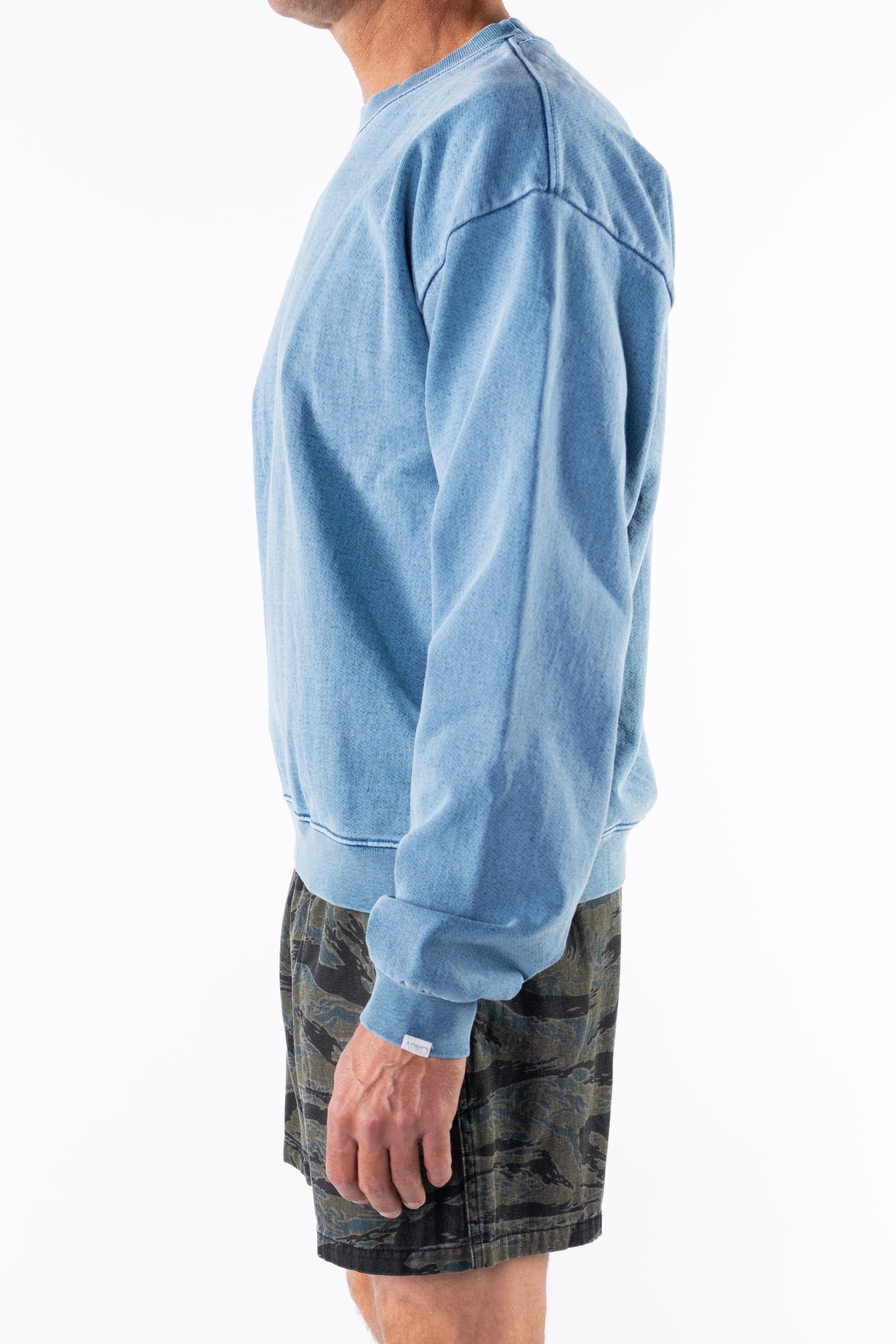 Side view of a person wearing a teal sweatshirt and ocean tiger camo day shorts on a white background