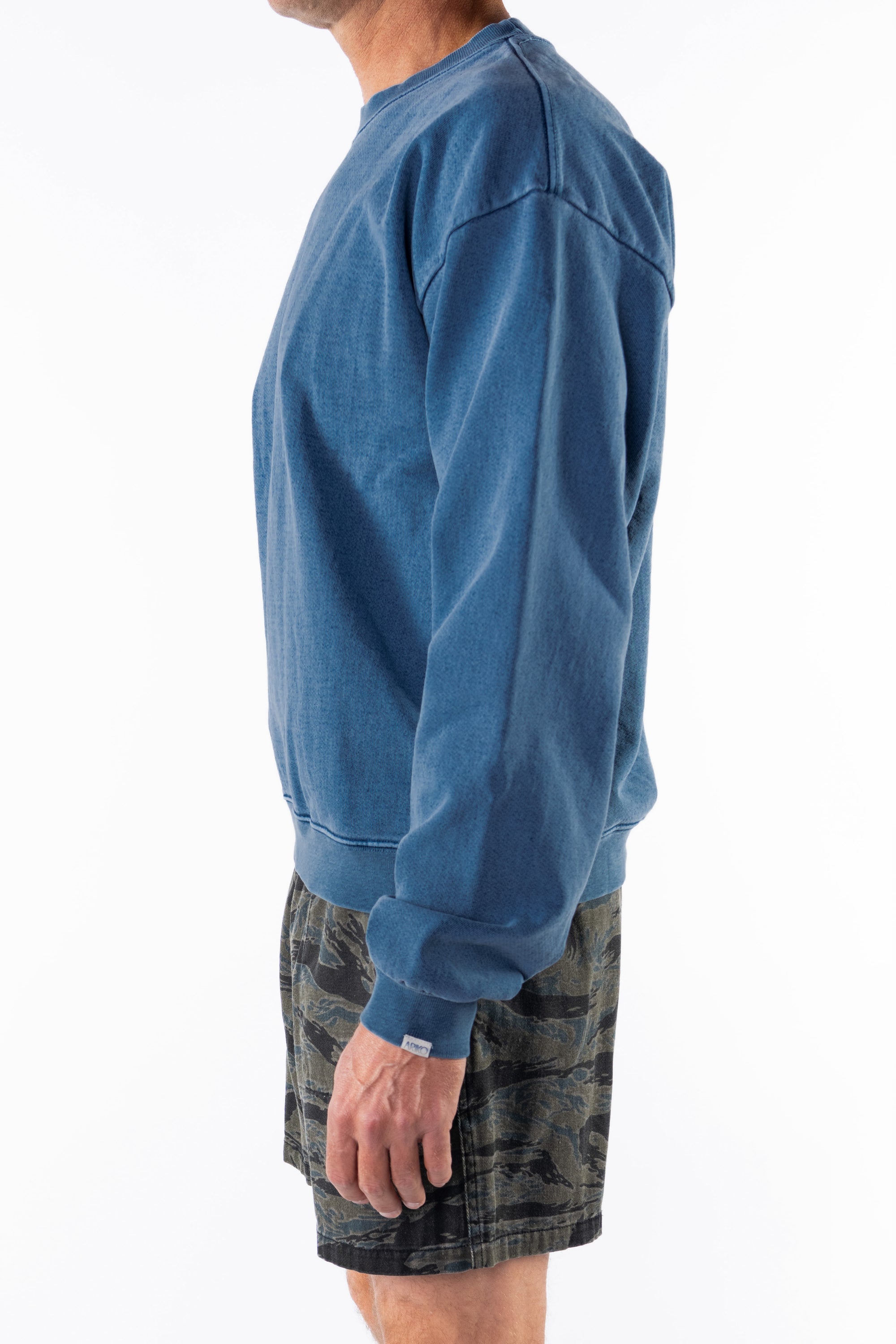 Person wearing a teal sweatshirt and ocean tiger camo shorts on a white background