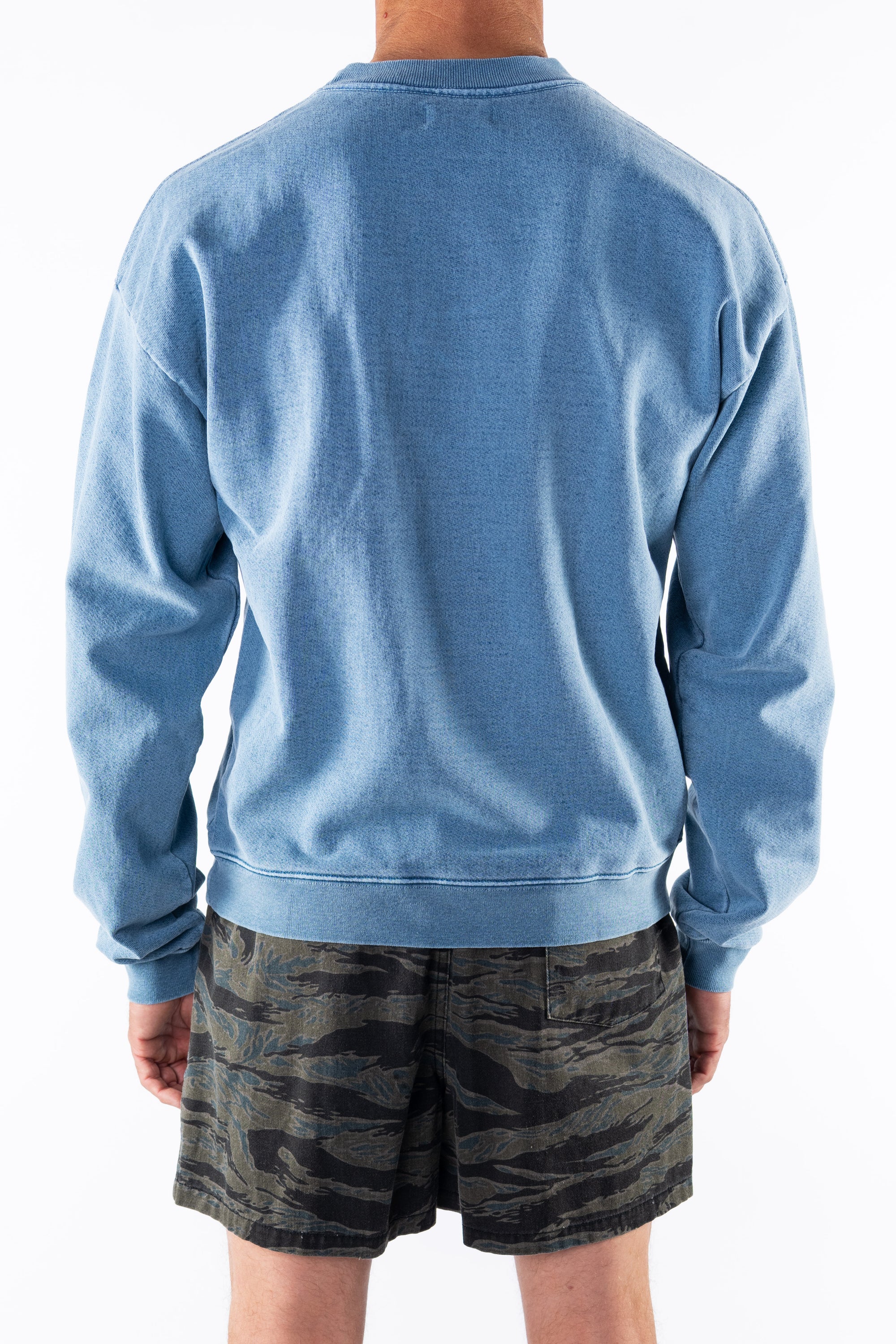 Back view of a person wearing a teal sweatshirt and ocean tiger camo day shorts on a white background
