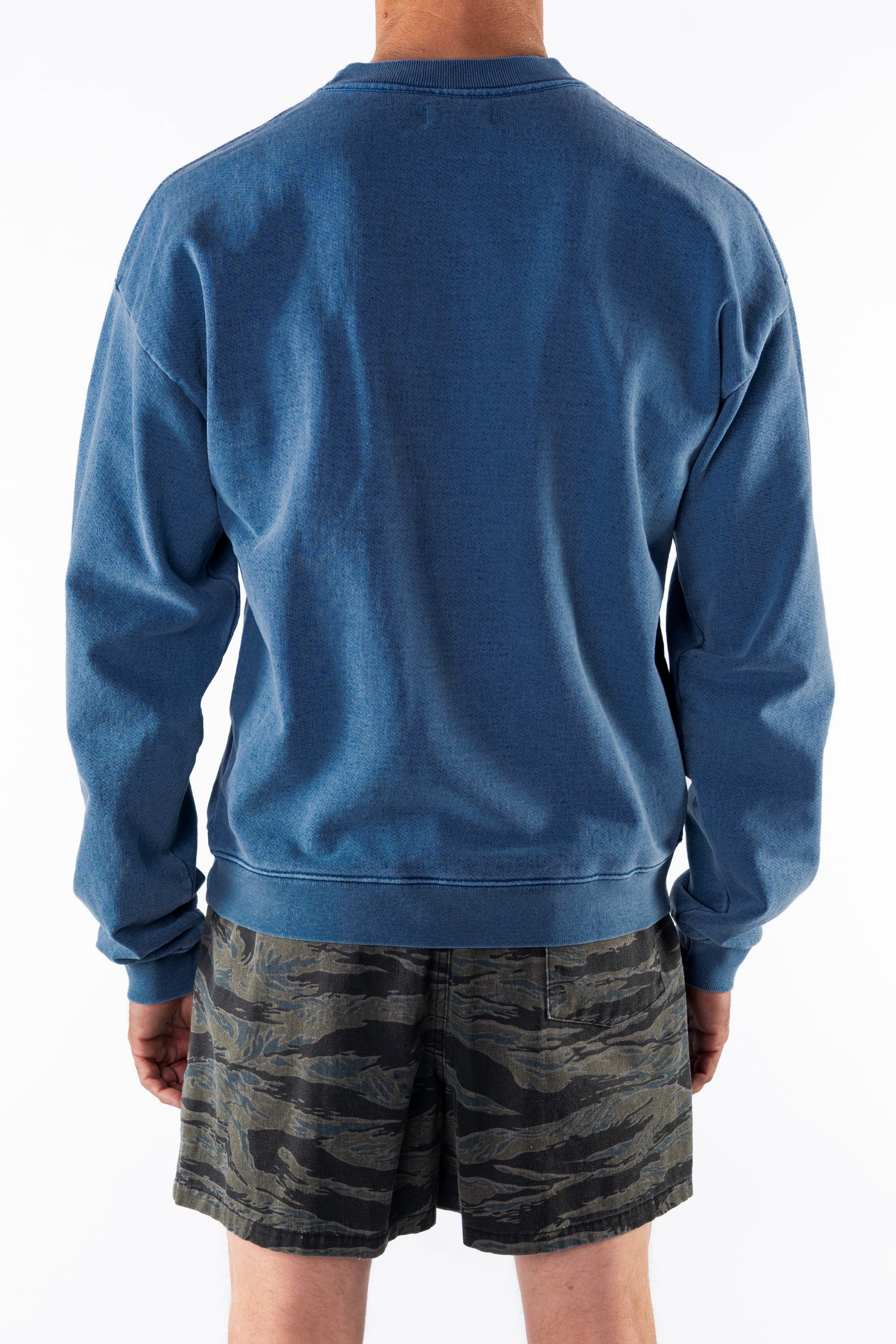 Back view of a person wearing a teal post surf crew sweatshirt and ocean tiger camouflage day shorts on a white background
