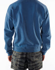 Back view of a person wearing a teal post surf crew sweatshirt and ocean tiger camouflage day shorts on a white background