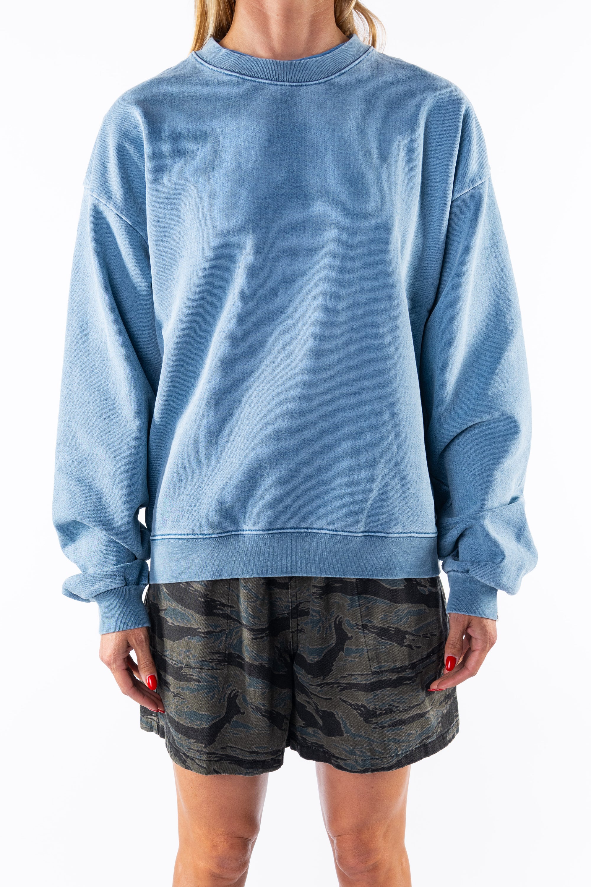 Woman wearing a teal sweatshirt and ocean tiger camo day shorts on a white background
