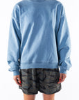 Woman wearing a teal sweatshirt and ocean tiger camo day shorts on a white background
