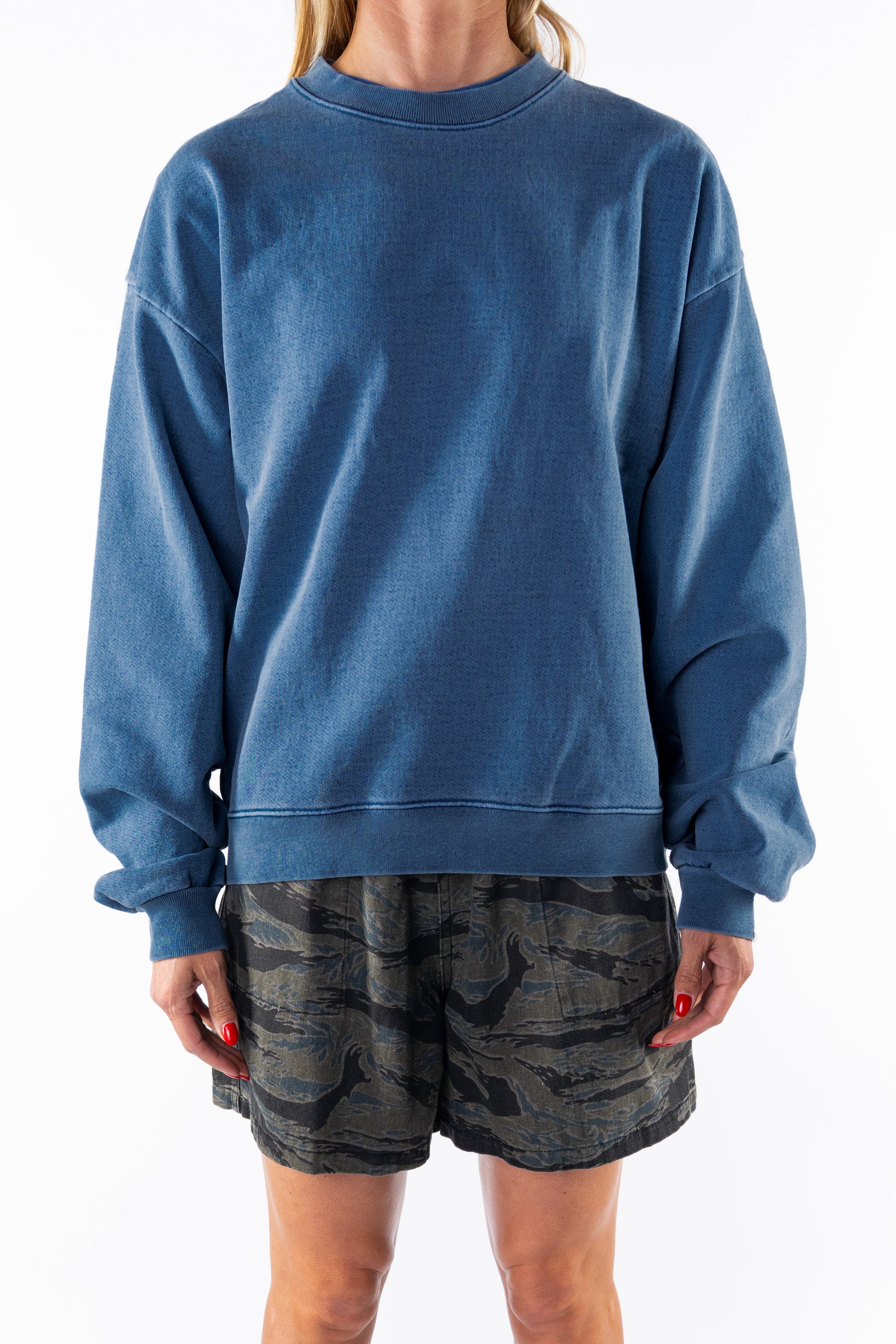 Woman wearing a teal post surf crew sweatshirt and ocean tiger camouflage day shorts on a white background