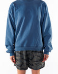 Woman wearing a teal post surf crew sweatshirt and ocean tiger camouflage day shorts on a white background