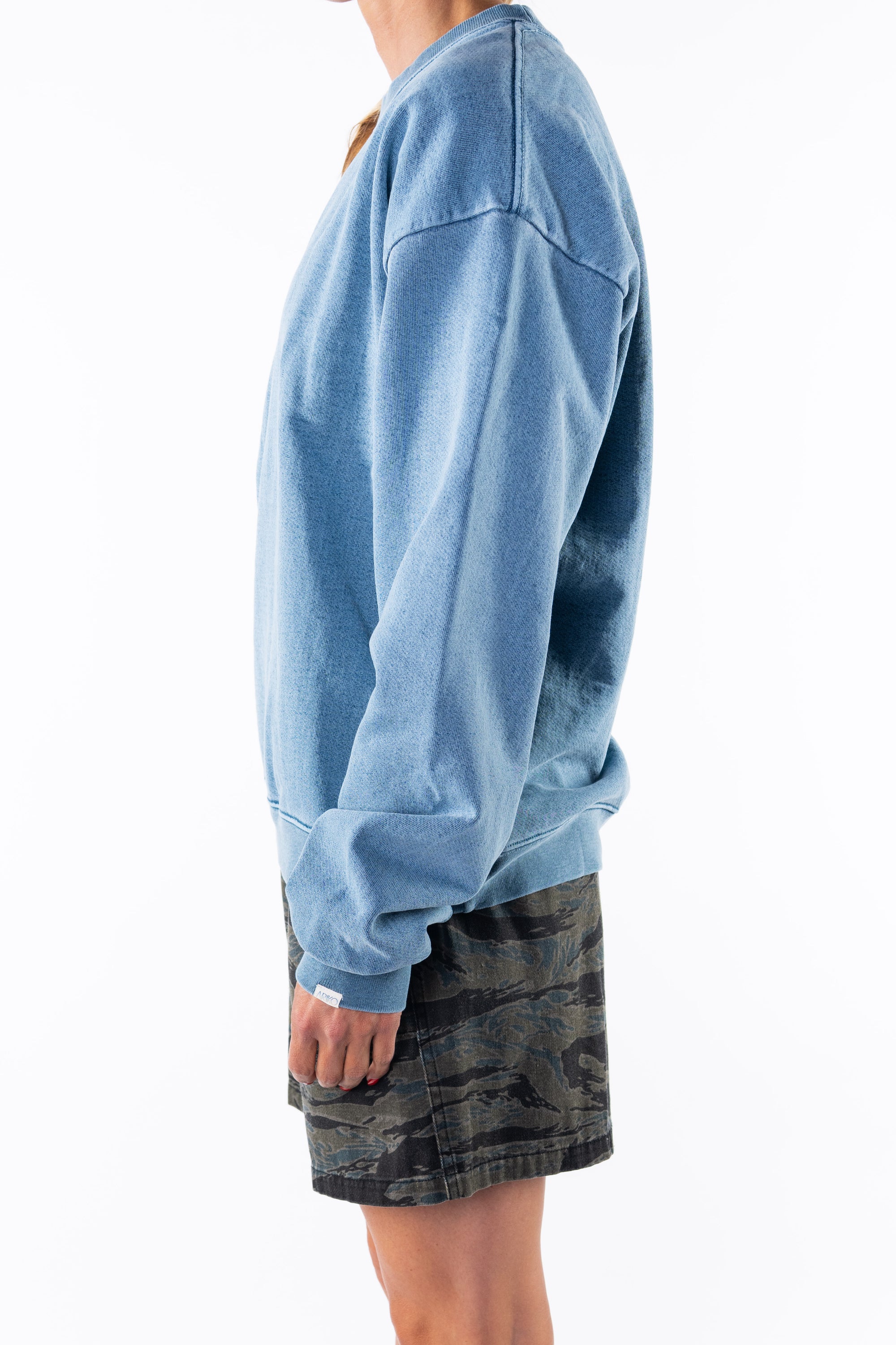 Side view of a woman wearing a teal sweatshirt and ocean tiger camo day shorts on a white background