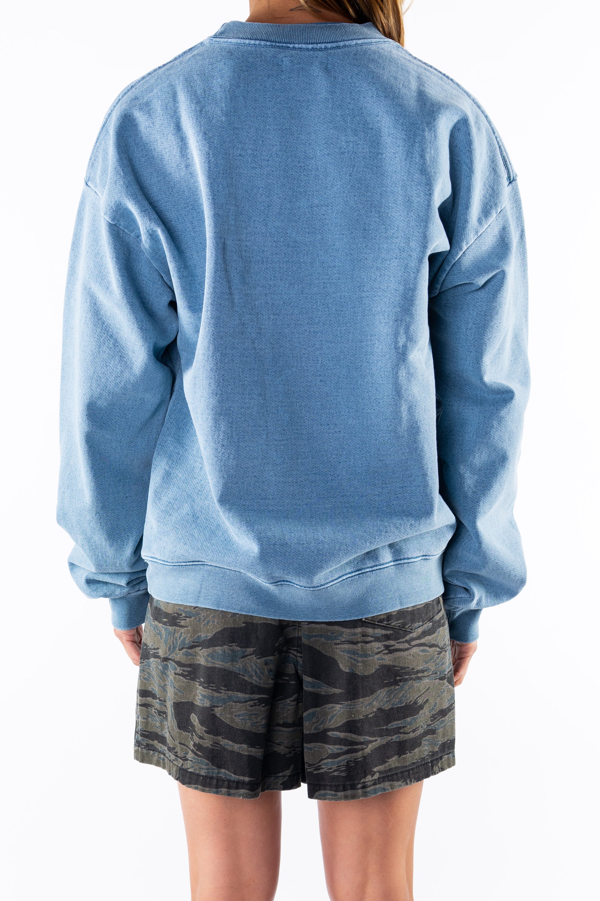 Back view of a woman wearing a teal sweatshirt and ocean tiger camo day shorts on a white background