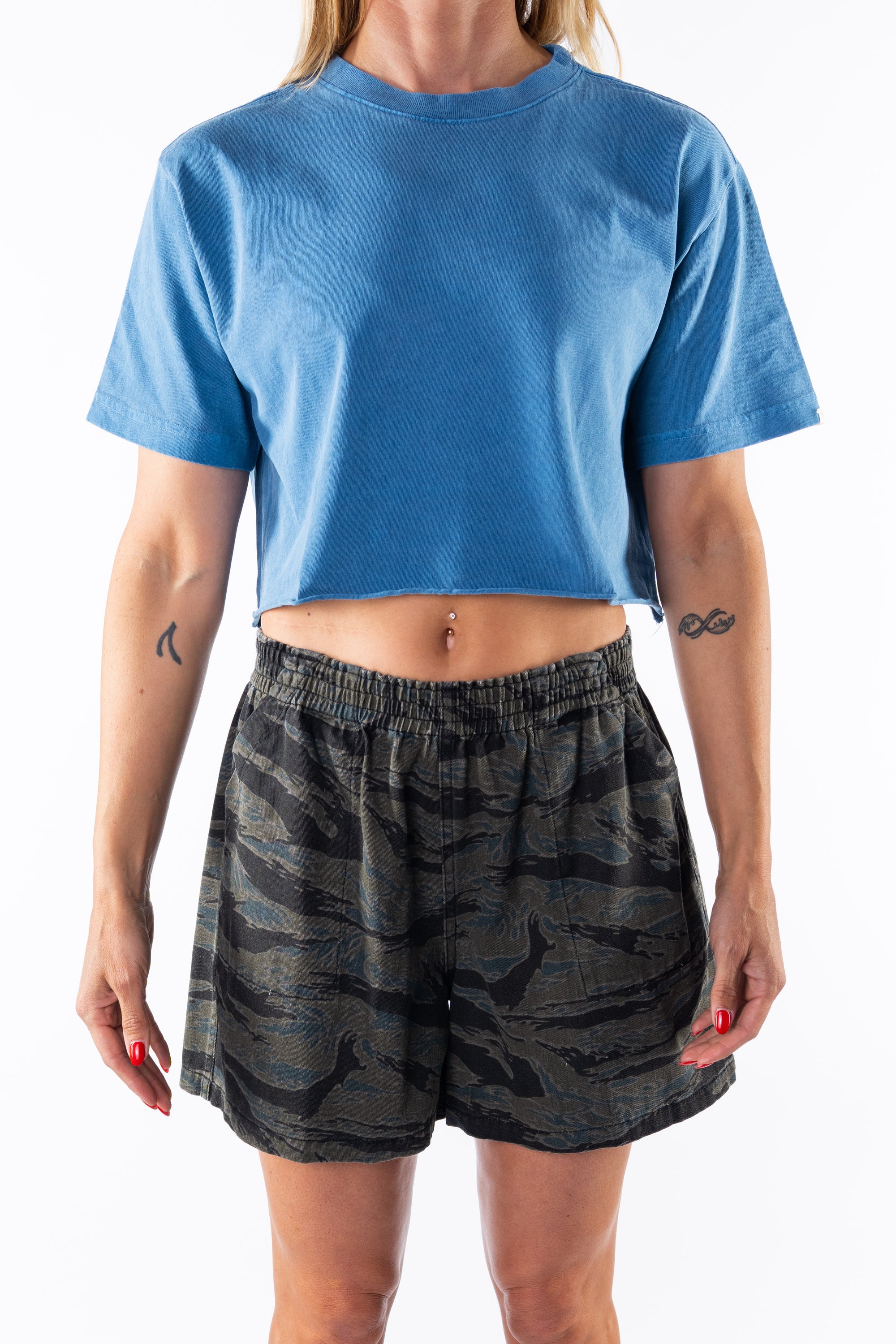 Woman wearing a teal crop t-shirt and ocean tiger camo day shorts on a white background