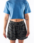 Woman wearing a teal crop t-shirt and ocean tiger camo day shorts on a white background