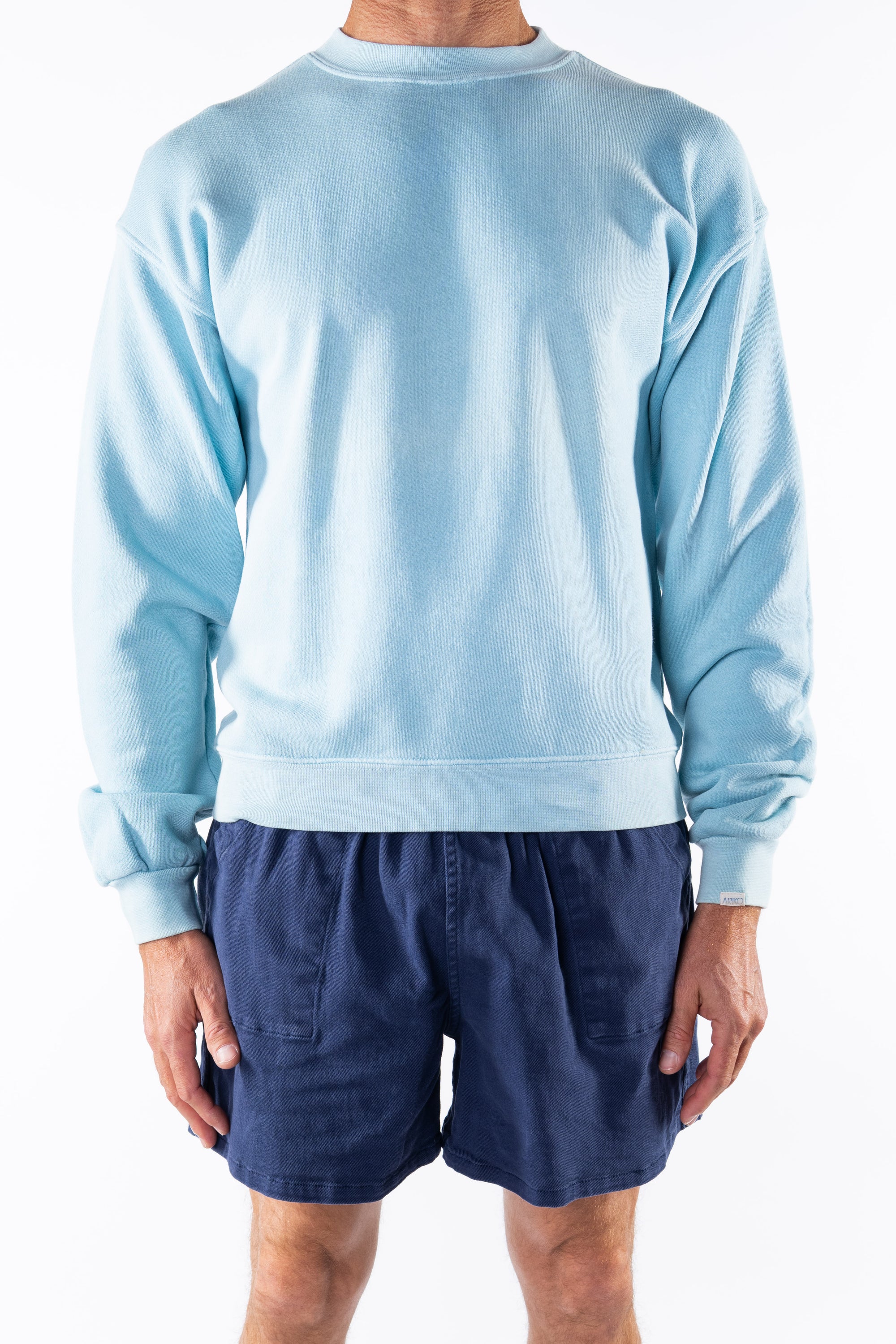 Person wearing a turquoise sweatshirt and navy day shorts on a white background
