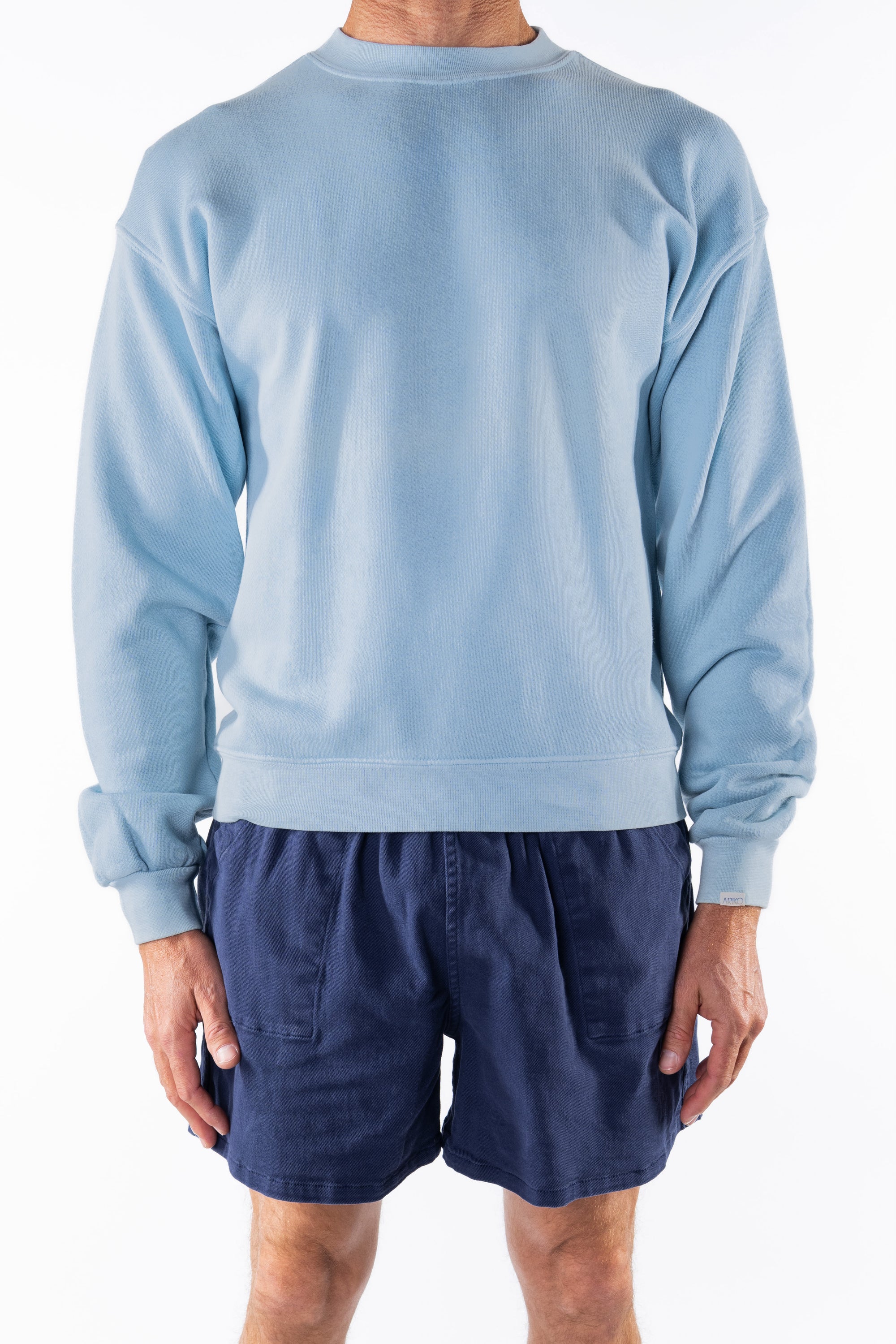 Person wearing a light blue ocean sweatshirt and navy day shorts on a white background