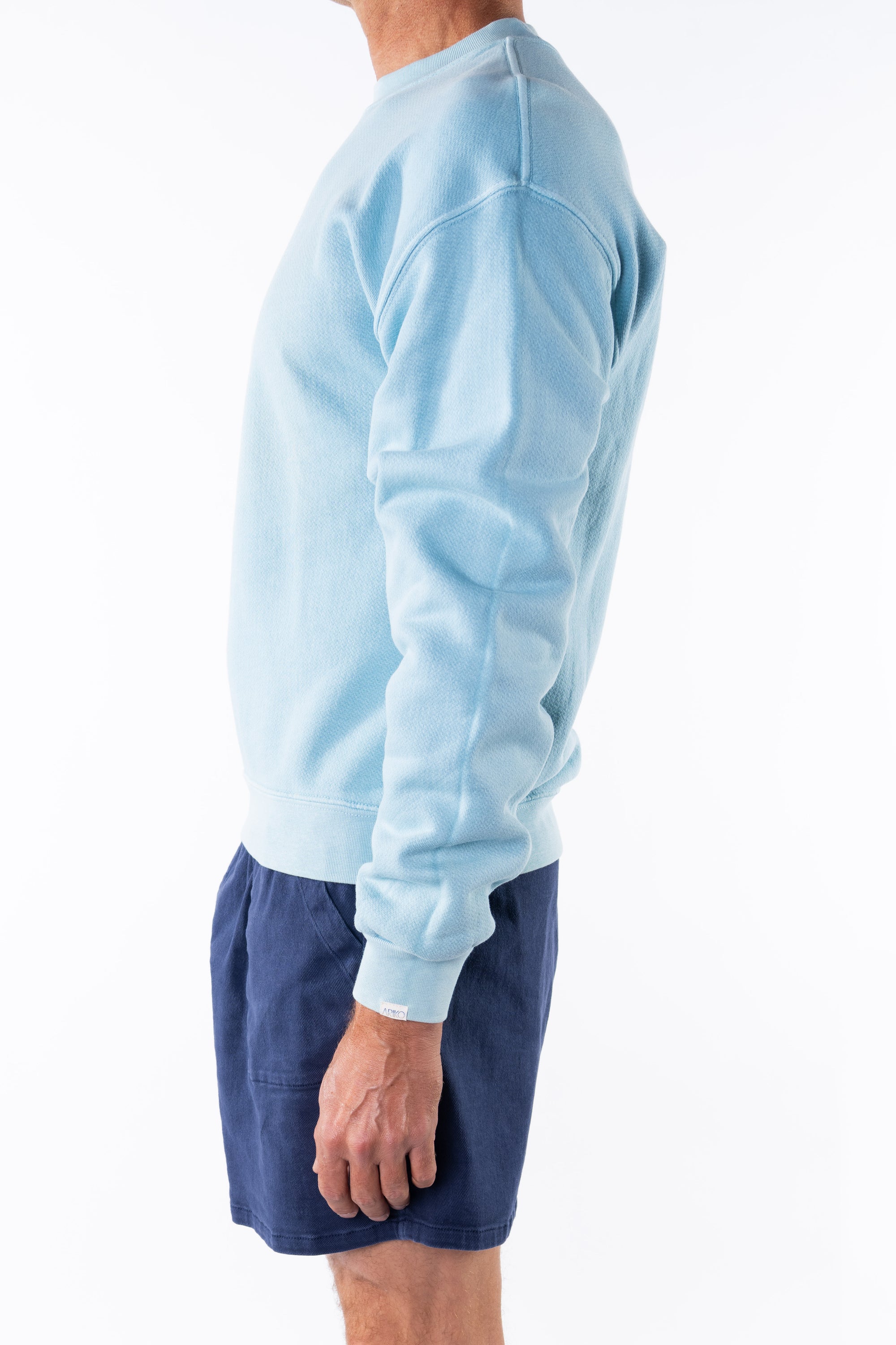 Person wearing a turquoise sweatshirt and navy day shorts on a white background