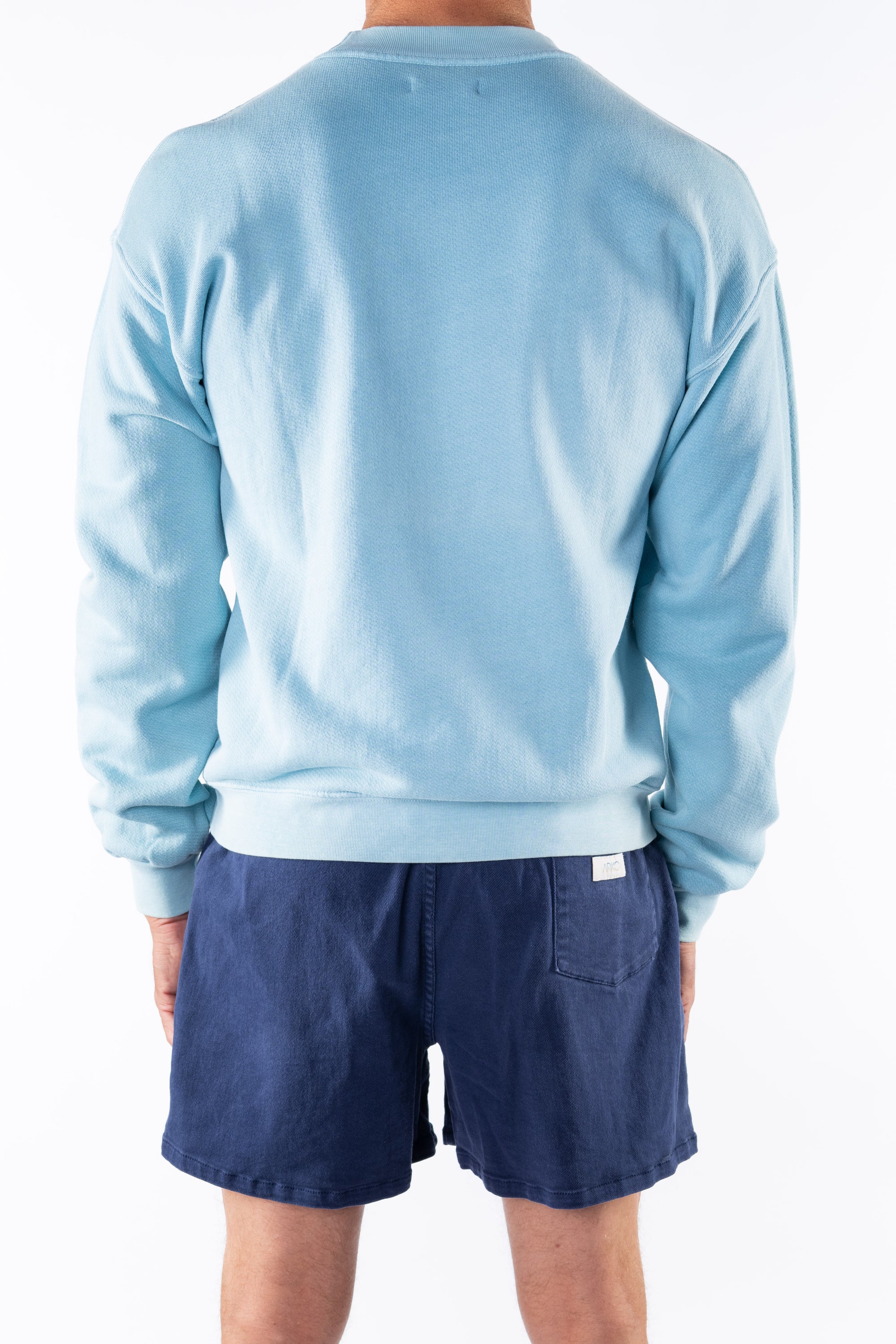 Back view of a person wearing a turquoise sweatshirt and navy day shorts on a white background