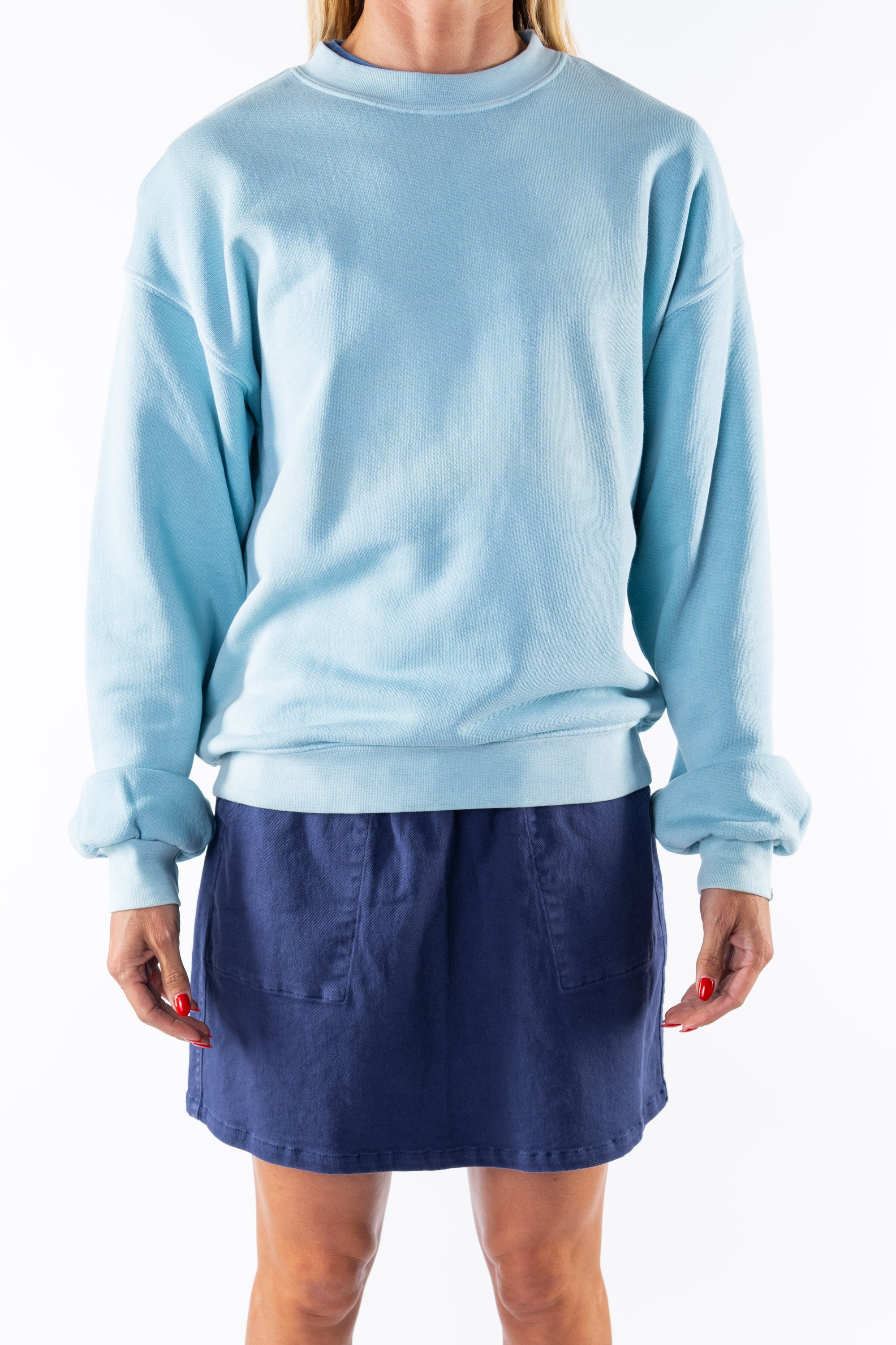 Person wearing a turquoise sweatshirt and navy day skirt on a white background