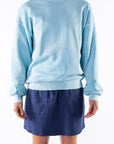 Person wearing a turquoise sweatshirt and navy day skirt on a white background