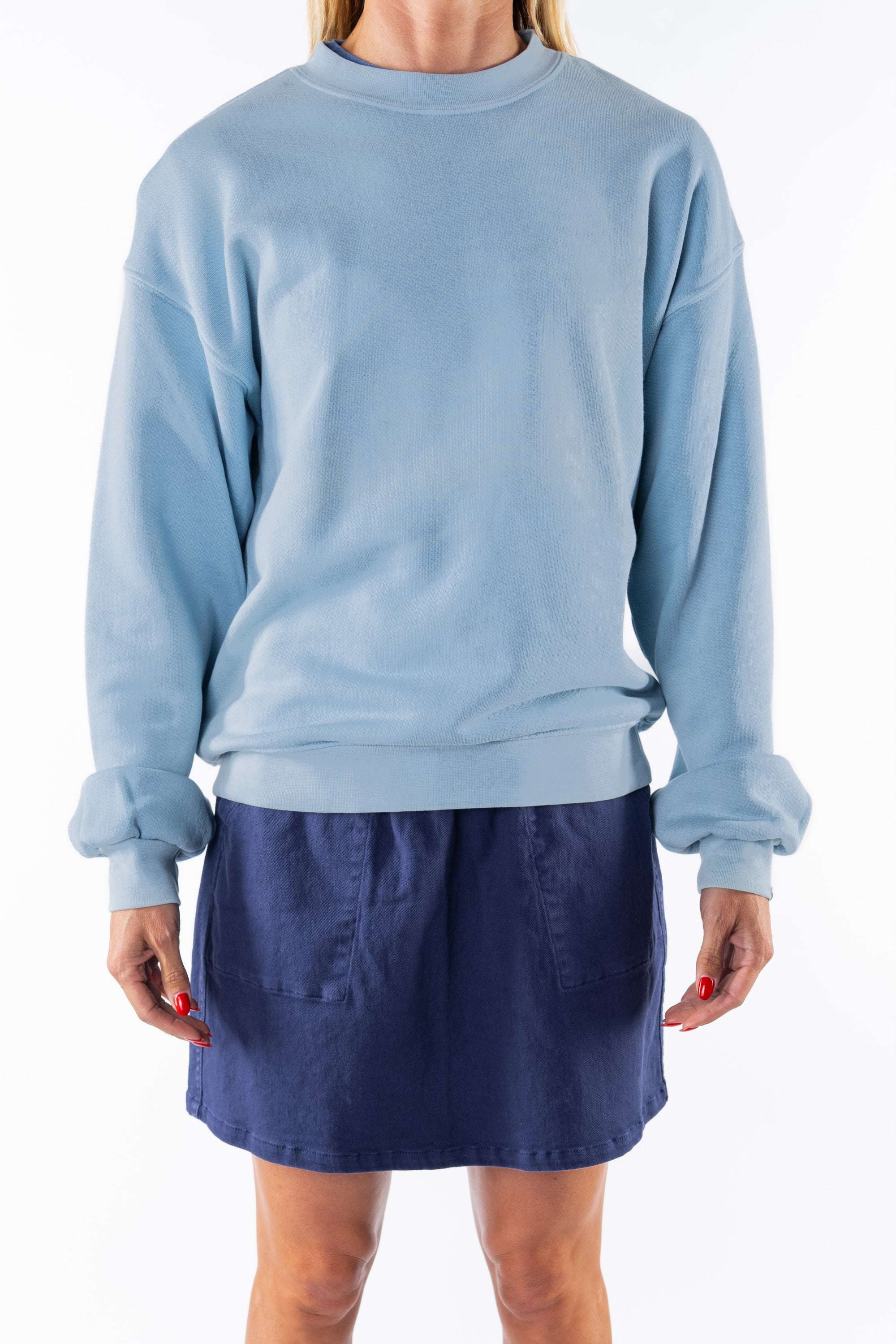 Woman wearing a light blue ocean sweatshirt and navy day skirt on a white background