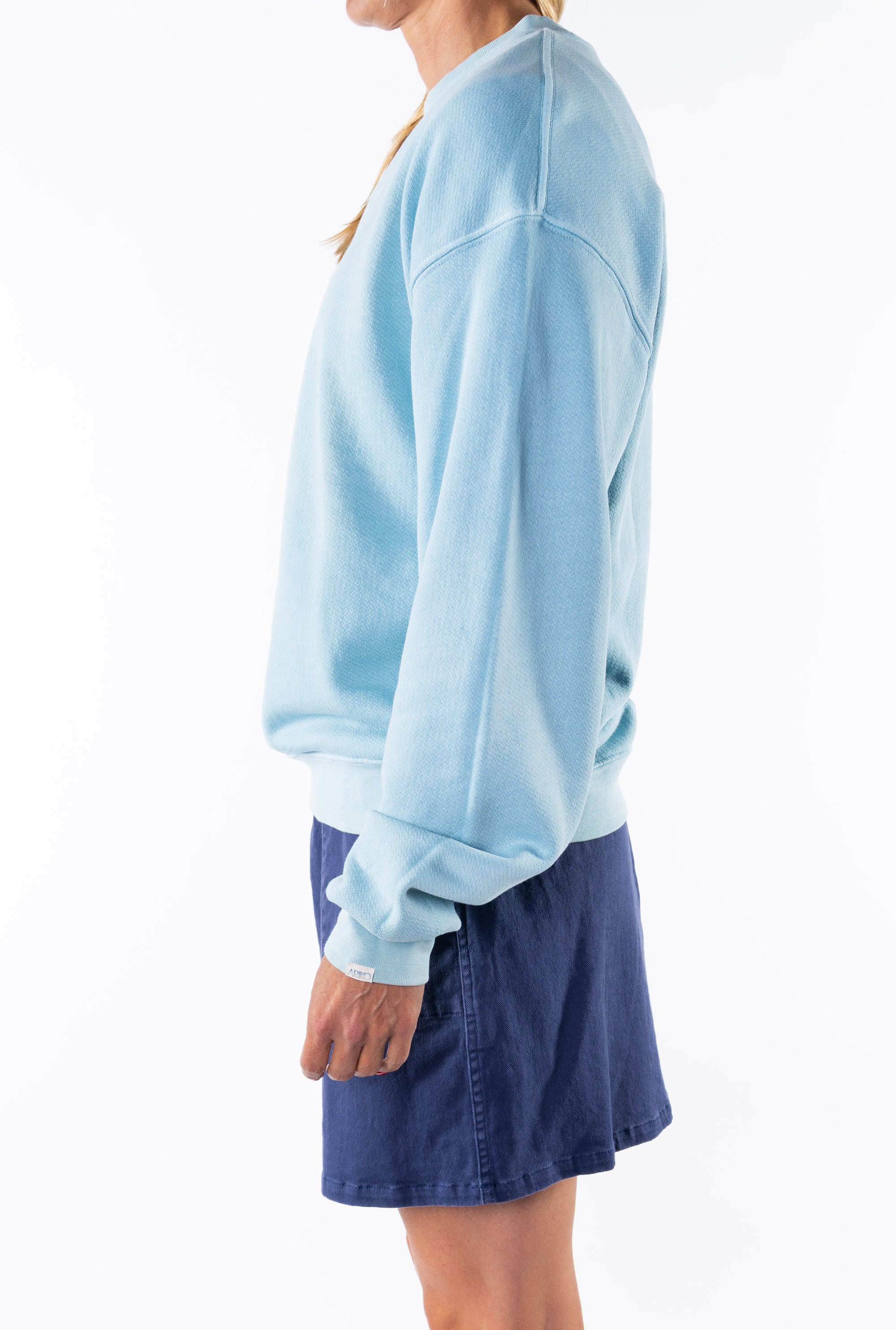 Side view of a woman wearing a turquoise sweatshirt and navy day shorts on a white background