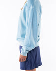Side view of a woman wearing a turquoise sweatshirt and navy day shorts on a white background