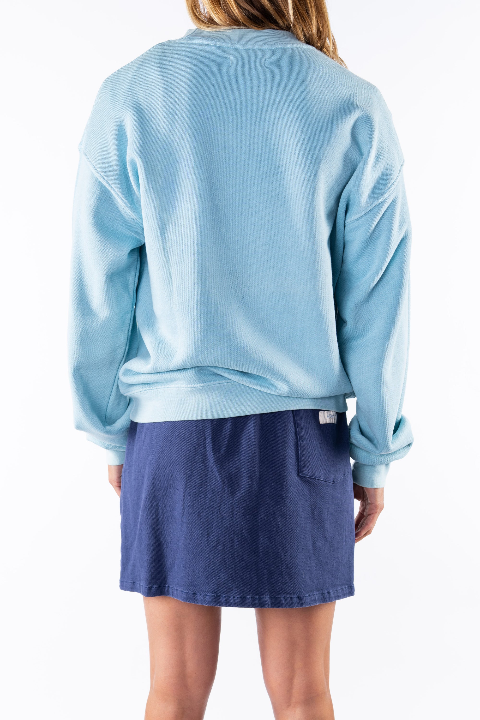 Back view of a woman wearing a turquoise sweatshirt and navy day skirt on a white background
