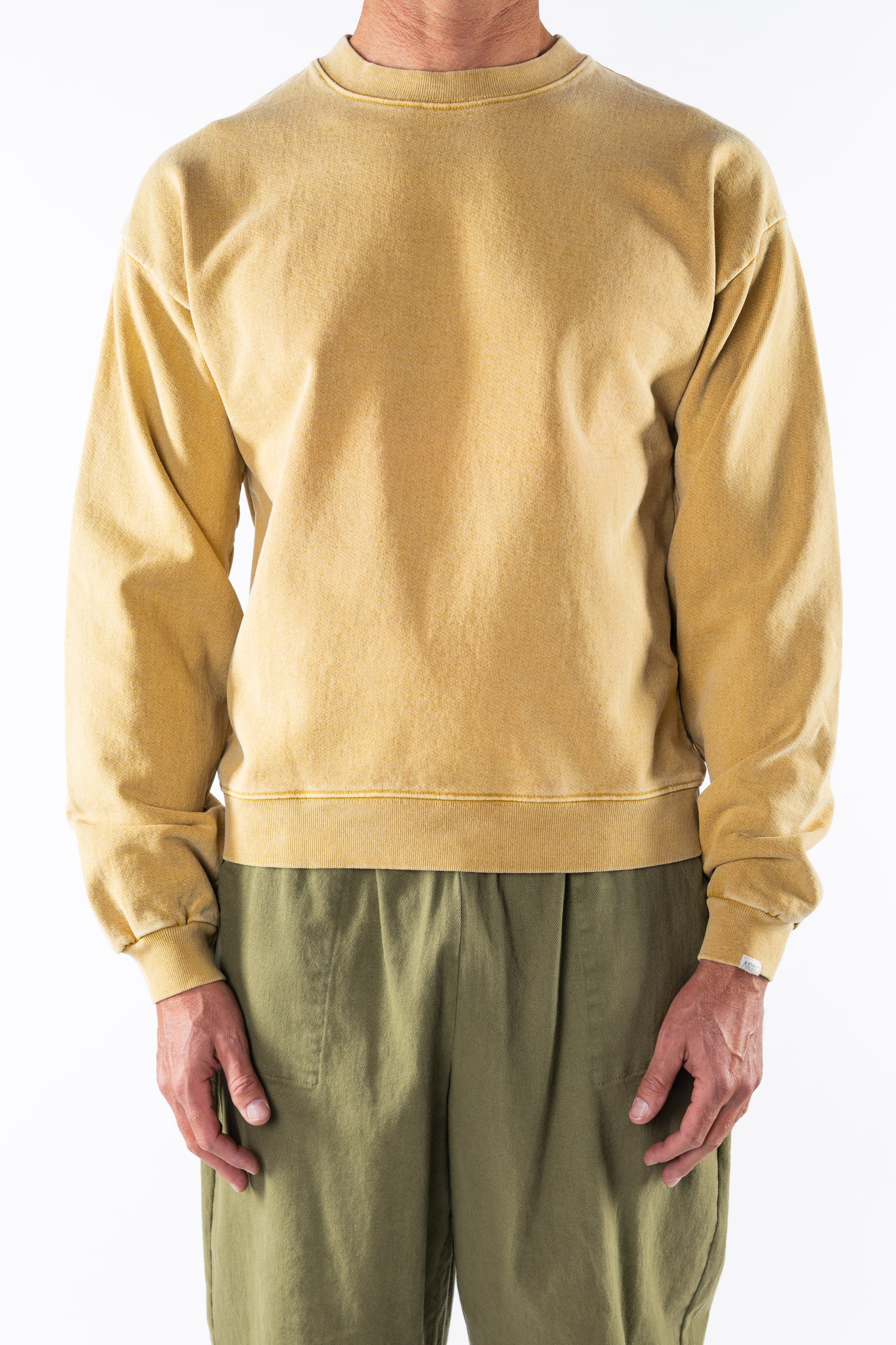 Person wearing a sunrise yellow sweatshirt and army green day pants on a white background
